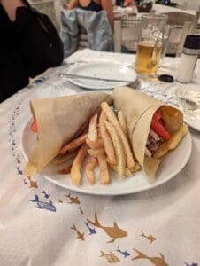 Sandwiches and Fries with Beer Plate with two wrapped sandwiches and fries, plus a glass of beer on a fish-patterned tablecloth.