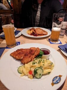 Schnitzel and Beer Feast Table with schnitzel, potato salad, cucumber, cranberry sauce, and two beers in a casual setting.