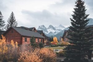 Row of wooden houses surrounded by autumn foliage and snow-covered mountains under cloudy sky