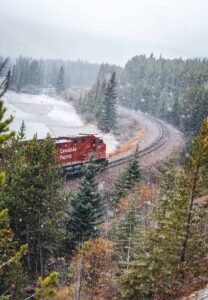 Red Canadian Pacific train on curved snow-covered tracks beside a frozen river and forest.