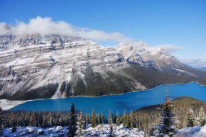 Blue lake surrounded by evergreen forest and snow-dusted rocky mountains under a clear sky