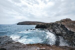 Rocky coastal cliffs enclosing a small cove with waves crashing under a cloudy sky
