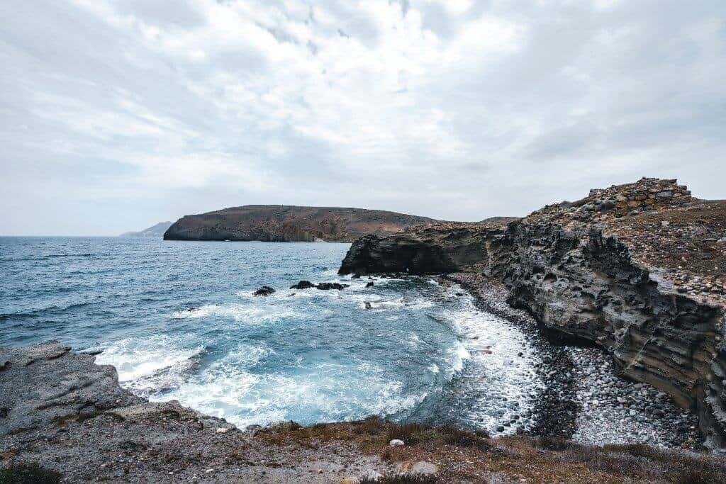 Rocky Coastline with Cliffs and Crashing Waves Rocky coastal cliffs enclosing a small cove with waves crashing under a cloudy sky