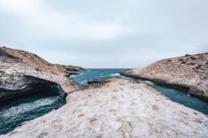 Rocky pale coastal formations with narrow channels of blue water leading to the sea under a cloudy sky