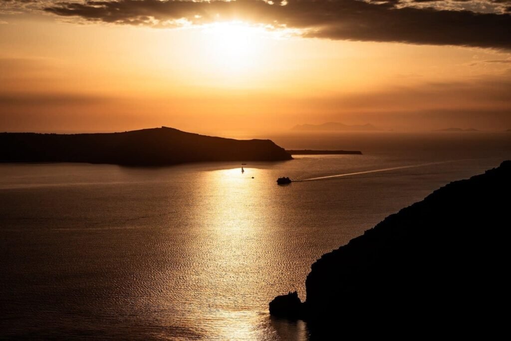 Sunset over water with silhouetted landmasses and two boats on the reflective surface.
