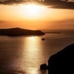 Sunset over water with silhouetted landmasses and two boats on the reflective surface.