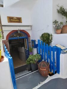 Entrance to Penelope's with blue gate, steps down, potted plants, and a wicker container.