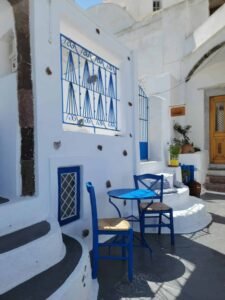 Outdoor seating area with blue table, two chairs, white walls, steps, and cushions.