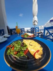 Omelette and salad with dressing on black plate on blue table with orange juice outdoors.