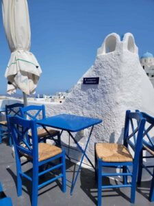 Outdoor seating with blue chairs and table near white stucco structure and closed umbrella.