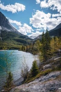 Turquoise lake with forested shores and snow-capped mountains under a partly cloudy sky