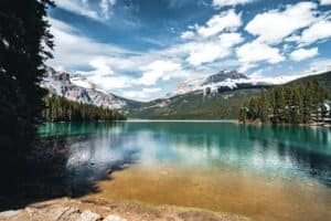 Turquoise mountain lake with evergreen forests and snow-capped peaks under a blue sky.