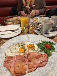 Plate with fried eggs, ham slices, arugula, cherry tomato, coffee, orange juice, and fruit jar.