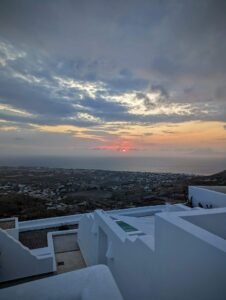 Sunset over Mediterranean coastal town with white buildings and partly cloudy sky.