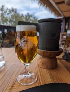 Glass of beer with foam on a wooden table next to a black container with a wooden base.