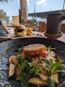 Salad with leafy greens, sliced fruit, sesame seeds, and breaded topping on black plate.