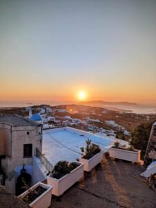Sunset over a coastal town with white buildings, blue dome church, and planter boxes.