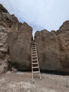 Wooden ladder leaning against a tall rocky cliff with a narrow gap at the top.