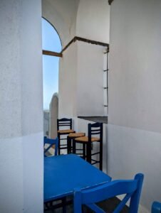 Outdoor seating area with blue wooden chairs and table against white stucco walls.