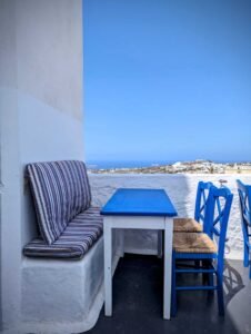 Outdoor seating with blue table, striped bench cushions, and blue chairs overlooking the sea.