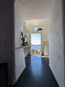 Narrow hallway with white walls leading to kitchenette and balcony overlooking sea and hills.