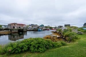 Harbor with colorful boats, wooden piers, fishing buildings, grassy shore, and cloudy sky.