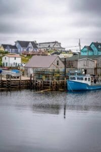 Blue fishing boat docked by wooden piers and buildings with colorful houses in the background.