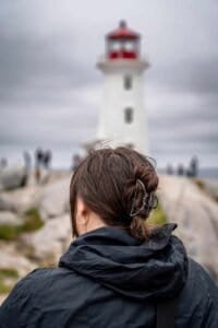 Person with dark hair bun and clip looking at white lighthouse with red top on cloudy day.
