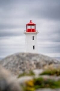White lighthouse with red top behind blurred rocks under cloudy sky