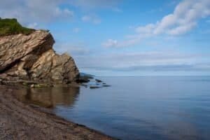Rocky Coastline with Sandy Shore and Calm Sea Rocky coastline with large rock formation, calm water, sandy shore, and partly cloudy sky.