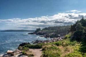 Rocky Coastal Cliffs with Forested Shoreline under Partly Cloudy Sky Rocky coastline with forested cliffs beside the ocean under a partly cloudy sky.
