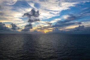 Body of water under a partly cloudy sky at sunset with distant city skyline on the horizon.