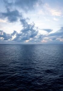 Ocean view under cloudy sky with distant city skyline on the horizon at twilight.