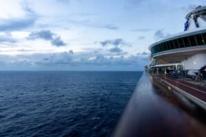 Ocean view from cruise ship deck with partly cloudy sky and lounge chairs.