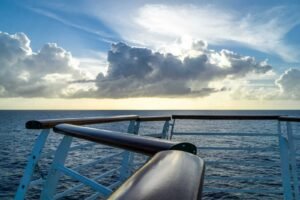 Ocean view from a ship's deck with wooden railing under partly cloudy sky near sunset or sunrise