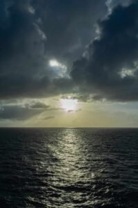 Ocean view with dark clouds and sunlight reflecting on the water surface.