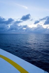 Ocean view under cloudy sky, seen from edge of white structure with yellow stripe.