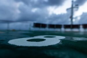 Wet surface with white number eight painted, blurred railing and mast under cloudy sky.