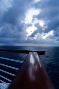 Ship railing close-up with ocean and overcast cloudy sky at dusk or early evening.